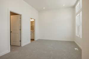 Unfurnished bedroom with light carpet, ensuite bathroom, and recessed lighting