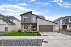 Contemporary house with stone siding, concrete driveway, a standing seam roof, a metal roof, and a front lawn