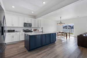Kitchen with white cabinetry, decorative backsplash, stainless steel appliances, hanging light fixtures, and open floor plan