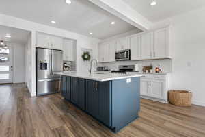 Kitchen with white cabinets, stainless steel appliances, beamed ceiling, decorative backsplash, and a center island with sink