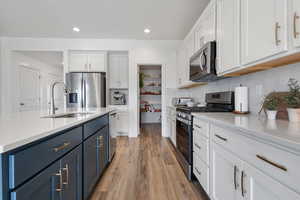 Kitchen featuring appliances with stainless steel finishes, light stone countertops, white cabinetry, light wood-type flooring, and backsplash
