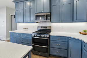 Kitchen featuring stainless steel appliances, blue cabinetry, light stone counters, and tasteful backsplash