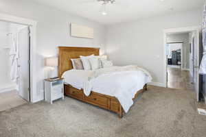 main floor primary Bedroom with light carpet, ceiling fan, and connected bathroom