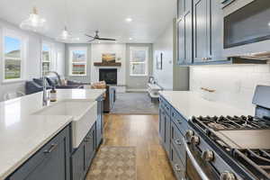 Kitchen with stainless steel appliances, light stone countertops, ceiling fan, light wood-type flooring, and a glass covered fireplace