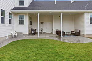 Rear view of house featuring a patio, a shingled roof, and a yard