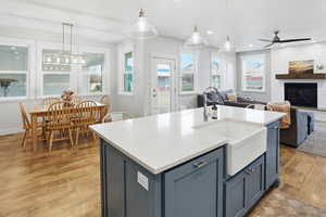 Kitchen featuring blue cabinetry, hanging light fixtures, light wood-type flooring, light stone counters, and open floor plan