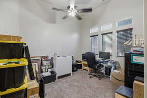 Office area featuring light colored carpet, a towering ceiling, and a ceiling fan