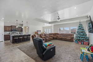 Living room featuring a raised ceiling, ceiling fan, a textured ceiling, recessed lighting, and stone finish floors