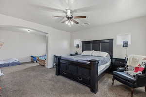 Carpeted bedroom featuring ceiling fan and arched walkways