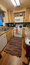 Kitchen featuring white appliances, backsplash, light wood-type flooring, tile counters, and brown cabinets