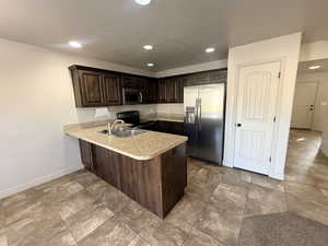 Kitchen with dark brown cabinetry, stainless steel appliances, light countertops, a peninsula, and recessed lighting