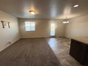 Spare room with a textured ceiling, a chandelier, light colored carpet, and light tile patterned floors