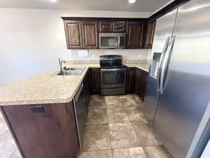 Kitchen featuring stainless steel appliances, a peninsula, dark brown cabinetry, light countertops, and recessed lighting