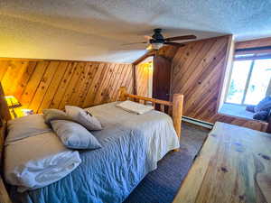 Bedroom featuring wooden walls, a ceiling fan, a textured ceiling, a baseboard heating unit, and access to outside