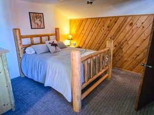 Carpeted bedroom with wood walls, a textured ceiling, and a ceiling fan