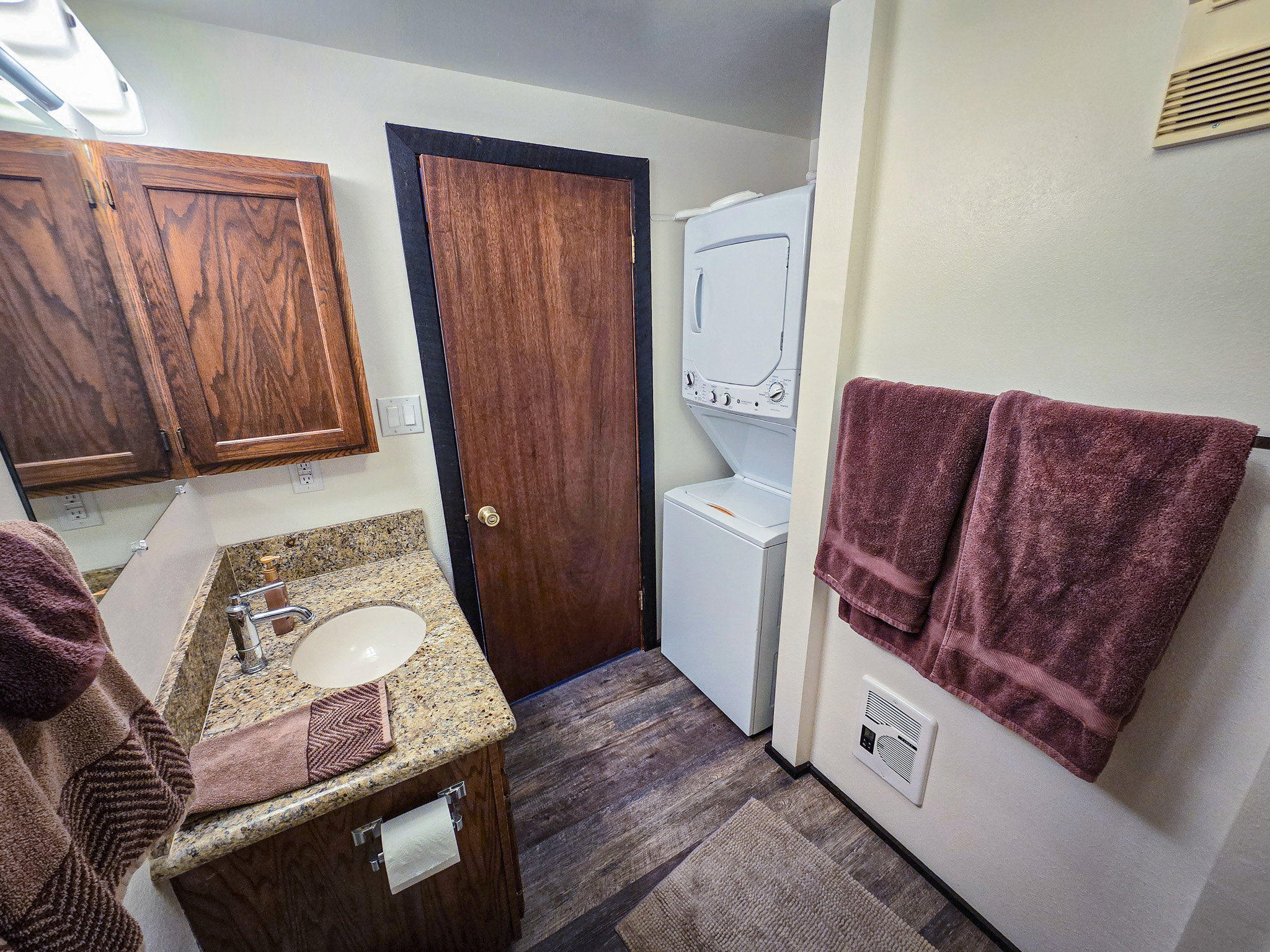 Half bathroom featuring vanity, stacked washing machine and dryer, dark wood finished floors, and heating unit