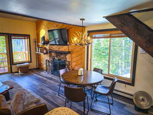 Dining area featuring a fireplace, a textured ceiling, dark wood finished floors, wooden walls, and a baseboard heating unit