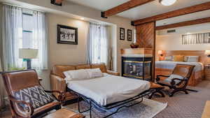 Carpeted bedroom with a fireplace, beamed ceiling, and recessed lighting