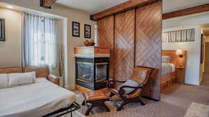 Carpeted bedroom featuring beamed ceiling, a fireplace, and wood walls