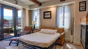 Bedroom with access to outside, beam ceiling, and a tiled fireplace
