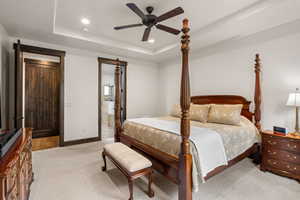 Bedroom featuring recessed lighting, a ceiling fan, a raised ceiling, light colored carpet, and ensuite bath