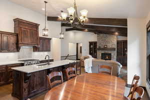 Kitchen with dark brown cabinetry, an island with sink, a stone fireplace, hanging light fixtures, and dark wood-style floors
