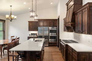 Kitchen featuring dark brown cabinetry, stainless steel appliances, pendant lighting, dark wood-style floors, and vaulted ceiling