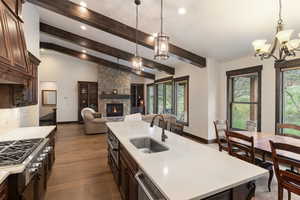 Kitchen featuring dark brown cabinetry, a chandelier, a center island with sink, and a stone fireplace
