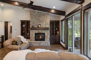 Living room with wood finished floors, a stone fireplace, recessed lighting, a ceiling fan, and built in shelves