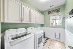 Washroom featuring wainscoting, separate washer and dryer, light tile patterned floors, and cabinet space