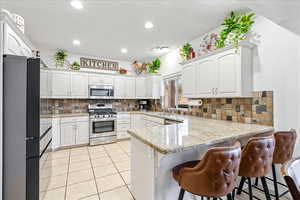Kitchen featuring a peninsula, appliances with stainless steel finishes, white cabinetry, recessed lighting, and a breakfast bar
