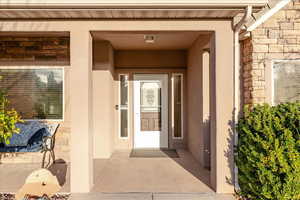 Doorway to property featuring stone siding, a porch, and stucco siding