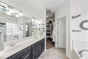 Full bath featuring a garden tub, a spacious closet, double vanity, and light wood-style floors