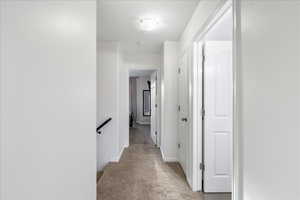 Hall with light colored carpet and an upstairs landing