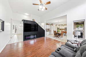Living area with light wood-style flooring, ceiling fan, a towering ceiling, and a glass covered fireplace