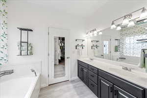 Bathroom with a bath, double vanity, and light wood-type flooring