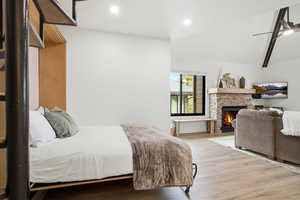 Bedroom featuring a stone fireplace, ceiling fan, light wood finished floors, recessed lighting, and lofted ceiling