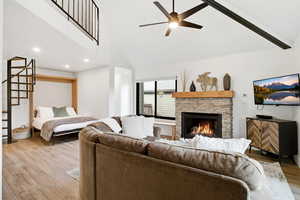 Living area featuring light wood-type flooring, a fireplace, high vaulted ceiling, a ceiling fan, and stairs