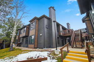 View of snowy exterior with stairs, a deck, and a chimney