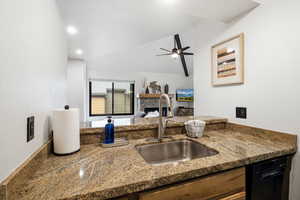Kitchen featuring a textured wall, dark stone counters, a fireplace, black dishwasher, and ceiling fan