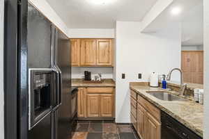 Kitchen with black appliances, light stone countertops, and stone tile flooring
