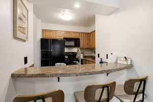 Kitchen featuring black appliances, a breakfast bar area, brown cabinets, a peninsula, and a textured wall