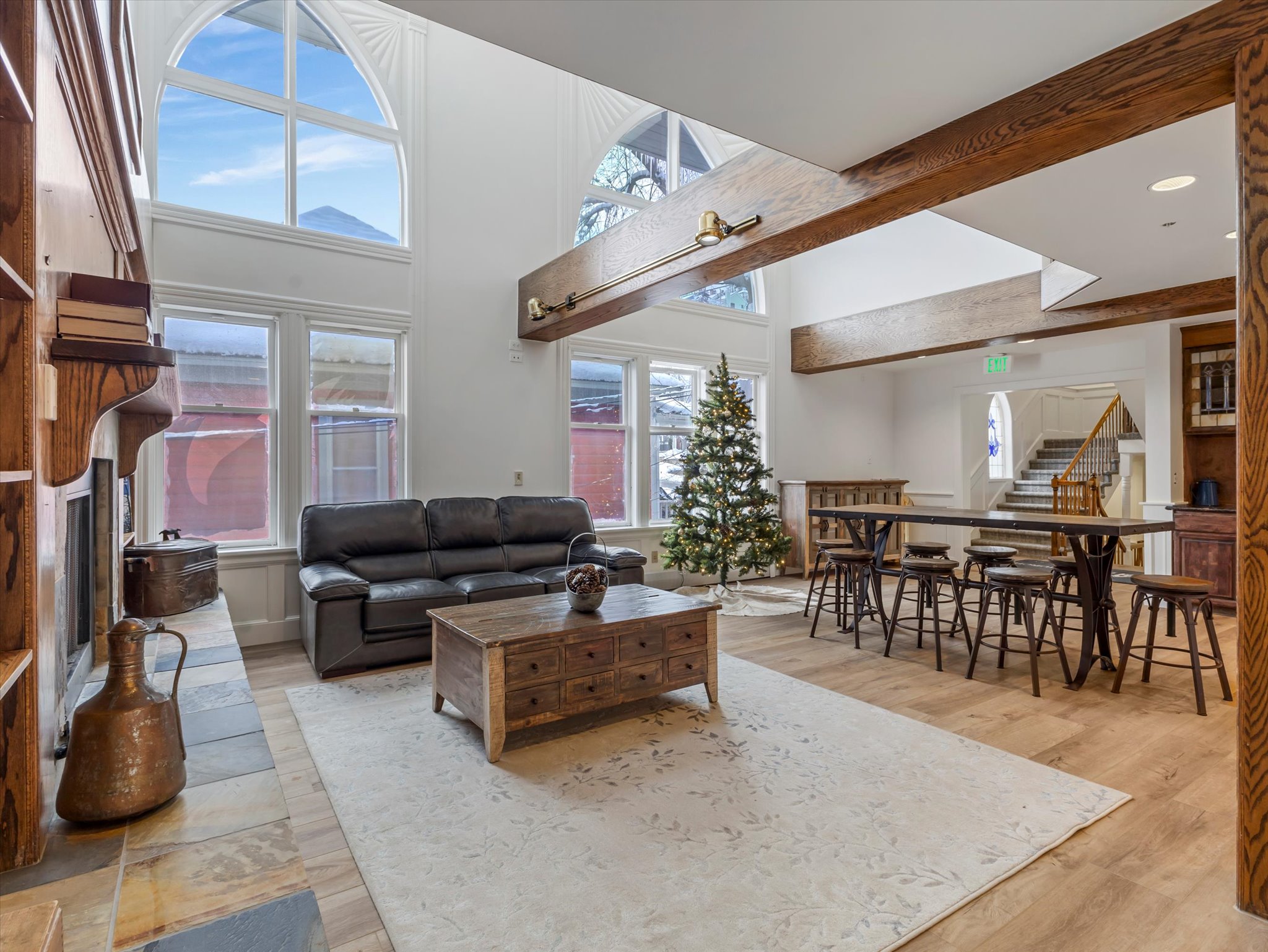 Living room with stairway, a fireplace, a towering ceiling, light wood-type flooring, and healthy amount of natural light