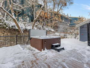 Snow covered deck with a hot tub and a fenced backyard