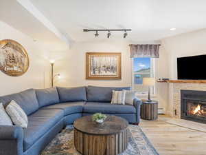 Living area with wood finished floors, rail lighting, a fireplace with flush hearth, and a baseboard heating unit