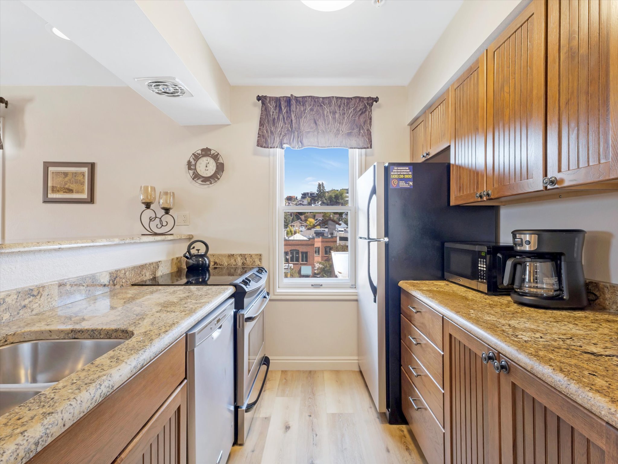 Kitchen with brown cabinetry, stainless steel appliances, light stone counters, and light wood-style flooring