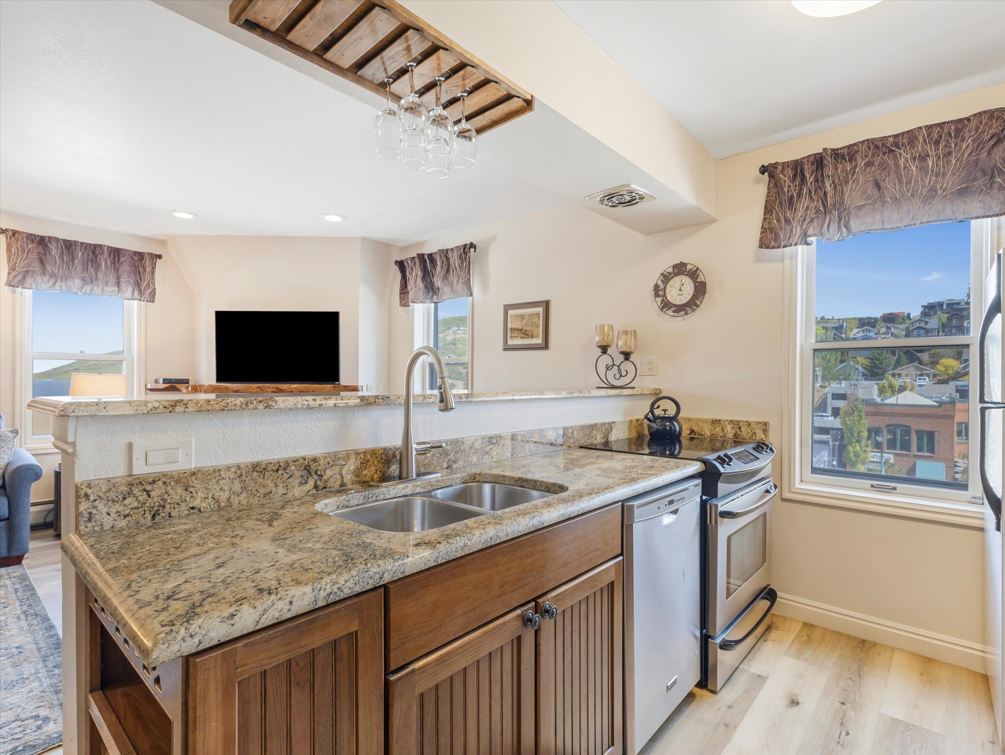 Kitchen featuring brown cabinetry, stainless steel appliances, open floor plan, light stone counters, and light wood-style floors