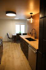 Kitchen with wooden counters, hanging light fixtures, stainless steel dishwasher, and light wood finished floors