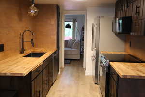 Kitchen with butcher block counters, electric range oven, hanging light fixtures, and dark cabinetry