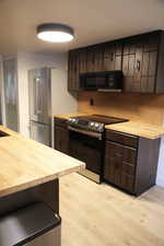 Kitchen featuring butcher block countertops, dark brown cabinets, stainless steel appliances, and light wood-style floors